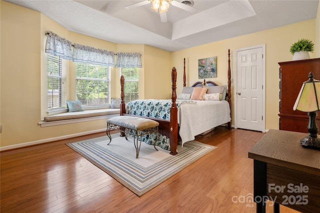 bedroom with baseboards, a ceiling fan, a raised ceiling, and wood finished floors
