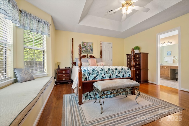 bedroom featuring baseboards, connected bathroom, wood finished floors, and a tray ceiling