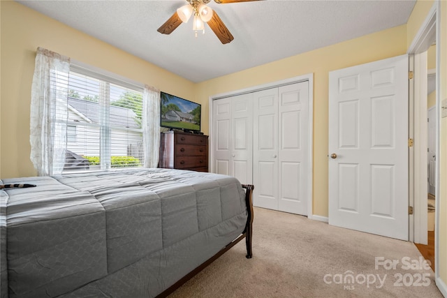 bedroom featuring a ceiling fan, a textured ceiling, light colored carpet, and a closet