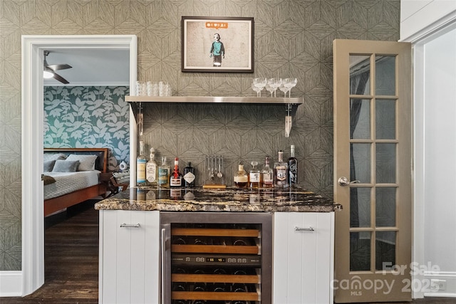 bar with a ceiling fan, wood finished floors, a bar, wallpapered walls, and beverage cooler