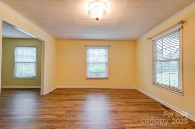 empty room featuring wood finished floors, visible vents, crown molding, and baseboards