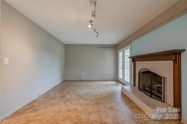 unfurnished living room with a fireplace, track lighting, baseboards, and light colored carpet