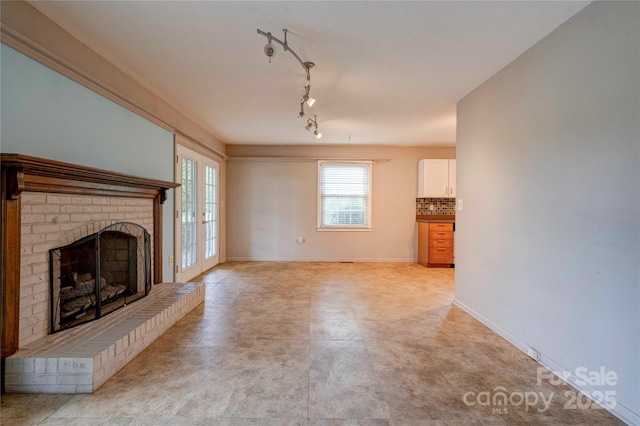 unfurnished living room with rail lighting, a brick fireplace, and baseboards