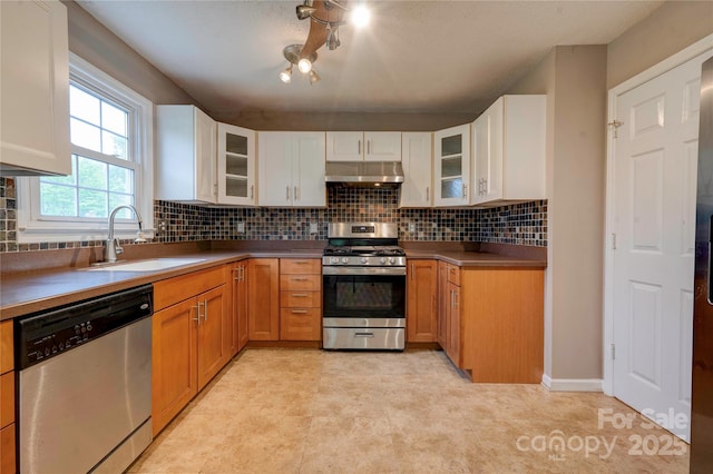 kitchen with white cabinets, a sink, backsplash, under cabinet range hood, and appliances with stainless steel finishes
