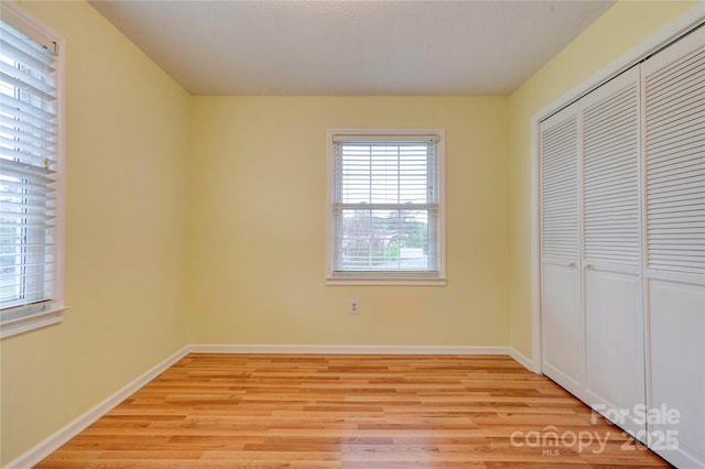 unfurnished bedroom featuring light wood finished floors, baseboards, and a closet