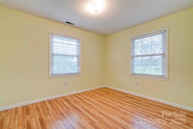 empty room with baseboards, wood finished floors, visible vents, and plenty of natural light