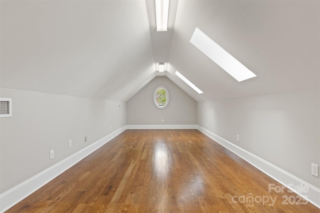 additional living space featuring lofted ceiling with skylight, visible vents, baseboards, and wood finished floors