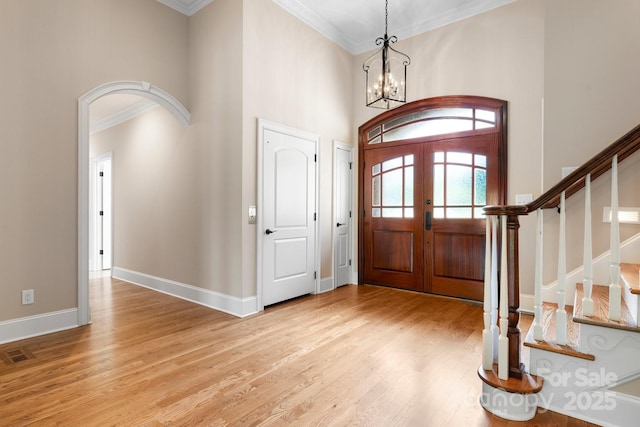 entrance foyer featuring stairway, light wood-style floors, arched walkways, french doors, and ornamental molding