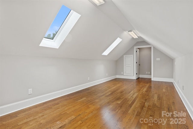 additional living space featuring baseboards, wood finished floors, and vaulted ceiling with skylight
