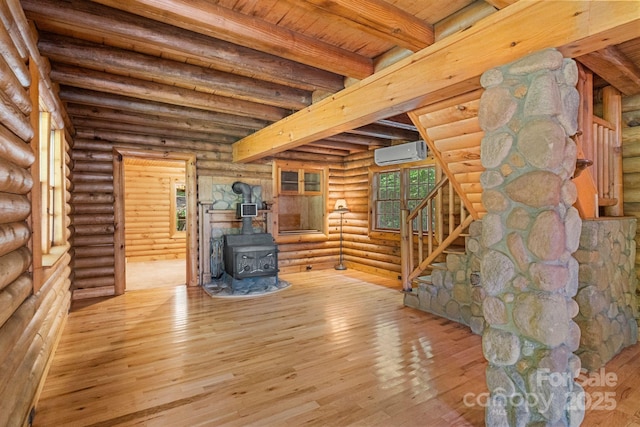 1154 Woodrow Pl, Lenoir, NC 28645 - unfurnished living room featuring an AC wall unit, beamed ceiling, a wood stove, hardwood / wood-style floors, and rustic walls