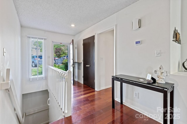 corridor featuring dark wood-style floors, recessed lighting, an upstairs landing, baseboards, and a textured ceiling