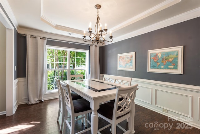 dining space featuring a chandelier, a raised ceiling, a decorative wall, crown molding, and dark wood-style floors