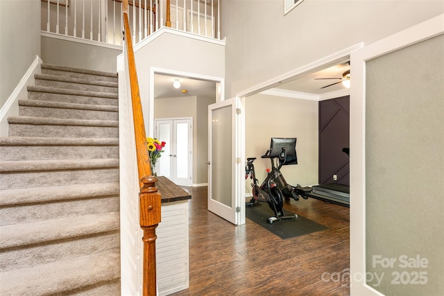 stairs with wood finished floors, a ceiling fan, a high ceiling, baseboards, and crown molding
