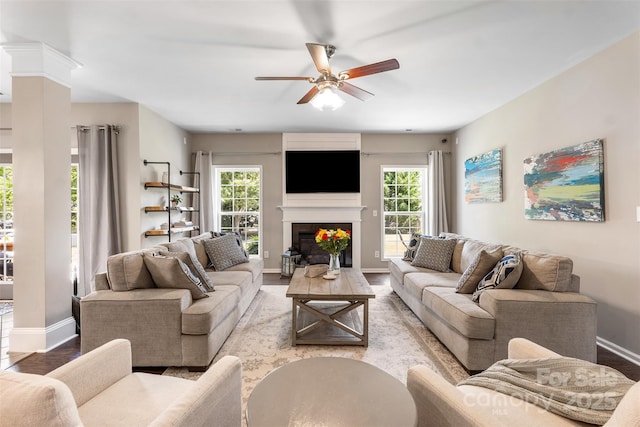 living area featuring a ceiling fan, baseboards, a fireplace, and wood finished floors