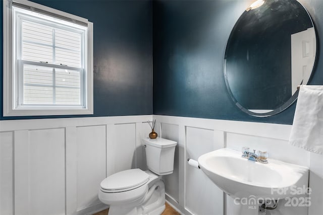 bathroom with a decorative wall, toilet, a wainscoted wall, and a sink