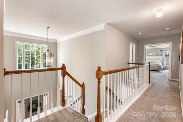 corridor with an upstairs landing, carpet flooring, a chandelier, crown molding, and baseboards