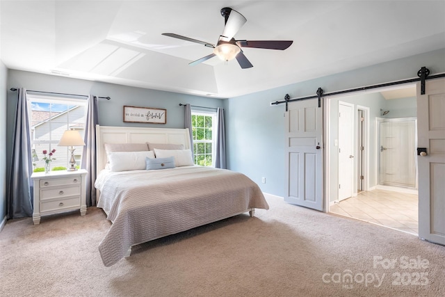 bedroom featuring a barn door, light carpet, vaulted ceiling, ceiling fan, and ensuite bath