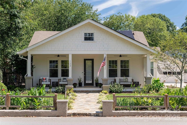bungalow-style house with a porch, a ceiling fan, a fenced front yard, and roof with shingles