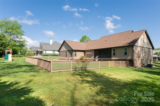 rear view of property featuring a lawn, a sunroom, a playground, and a fenced backyard