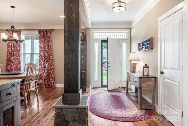 foyer entrance featuring baseboards, a chandelier, ornamental molding, and wood finished floors