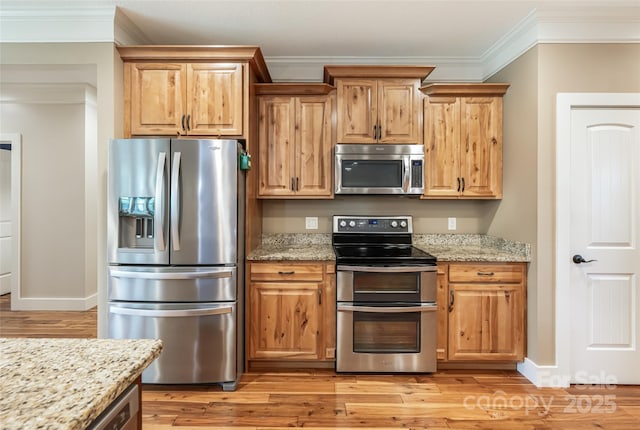 kitchen with crown molding, stainless steel appliances, light stone countertops, and light wood-style flooring
