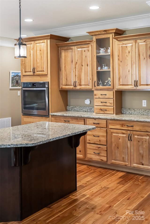 kitchen featuring a breakfast bar area, stainless steel oven, ornamental molding, and light wood-style flooring