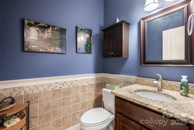 bathroom featuring vanity, wainscoting, toilet, and tile walls