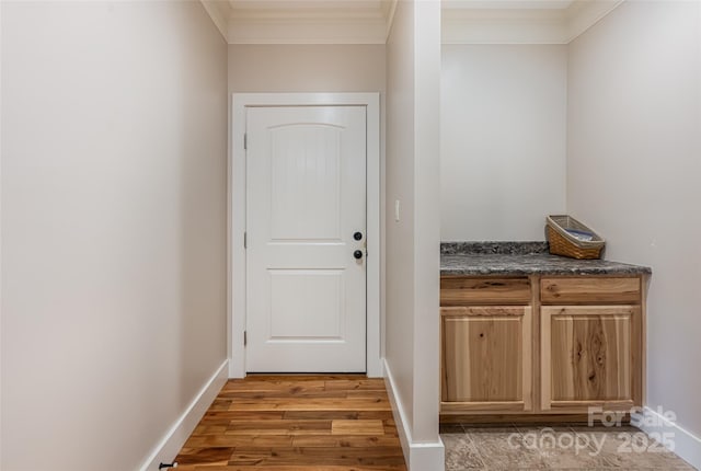 doorway featuring crown molding, baseboards, and light wood finished floors