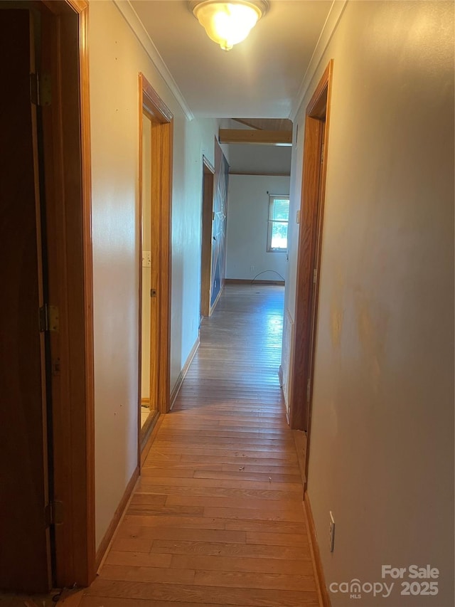 hall with light wood-style flooring, ornamental molding, and baseboards