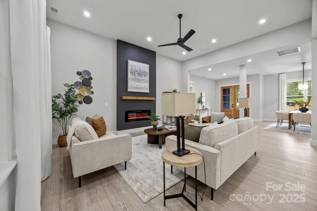 living area with a large fireplace, visible vents, light wood-type flooring, recessed lighting, and a ceiling fan