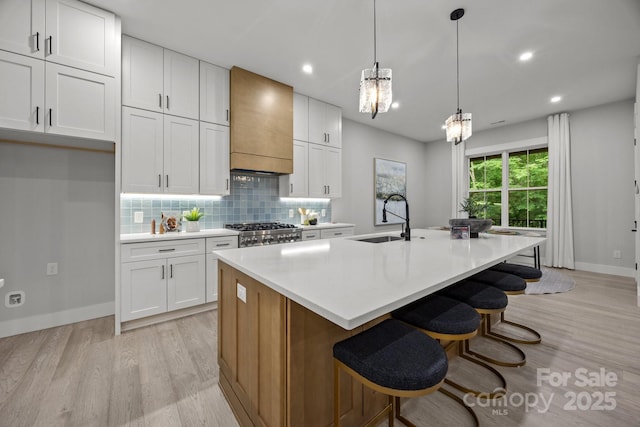kitchen with custom exhaust hood, a sink, baseboards, and light wood-type flooring