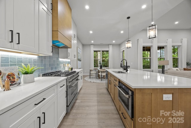 kitchen with decorative backsplash, appliances with stainless steel finishes, a large island with sink, a sink, and light wood-type flooring