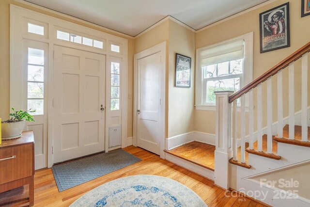 entrance foyer with baseboards, crown molding, stairs, and light wood finished floors