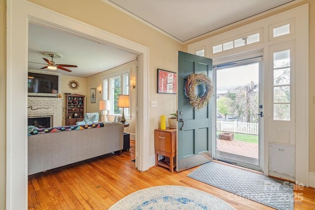 foyer with crown molding, light wood-style flooring, ceiling fan, a fireplace, and baseboards