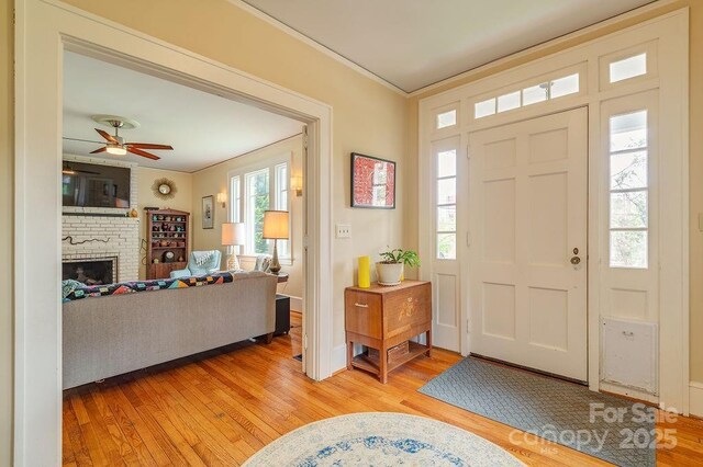 entryway with light wood-style flooring, a wealth of natural light, ornamental molding, and a fireplace