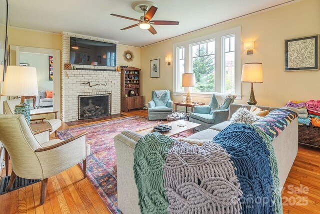 living room featuring wood finished floors, visible vents, a ceiling fan, ornamental molding, and a brick fireplace