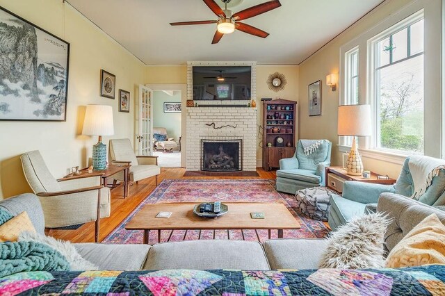 living area featuring a fireplace, crown molding, wood finished floors, and a ceiling fan