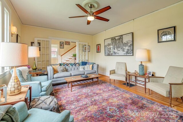 living area with stairway, ceiling fan, baseboards, and wood finished floors