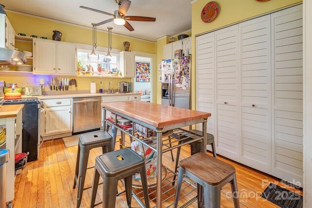 kitchen featuring light countertops, a ceiling fan, light wood-style floors, crown molding, and appliances with stainless steel finishes
