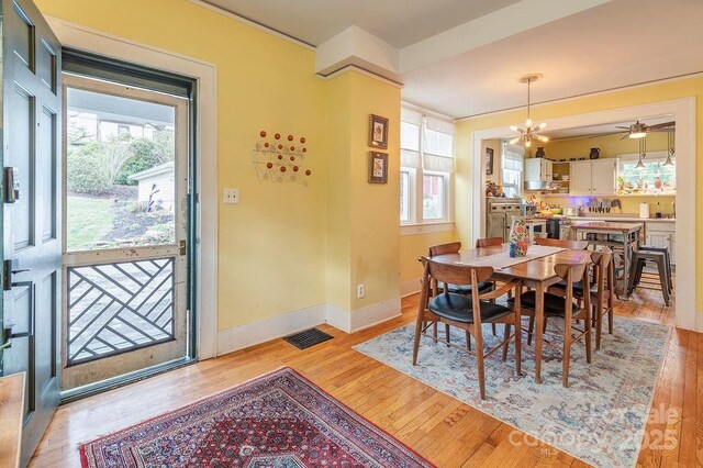 dining space with light wood-type flooring, baseboards, visible vents, and ceiling fan with notable chandelier
