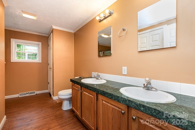 bathroom featuring wood finished floors, toilet, ornamental molding, double vanity, and a textured ceiling