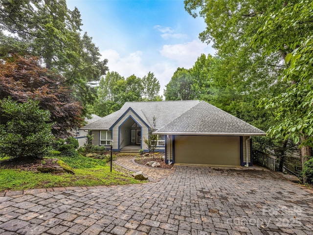 ranch-style home with an attached garage, roof with shingles, and decorative driveway
