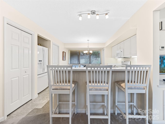 kitchen with an inviting chandelier, white cabinetry, white appliances, a peninsula, and a breakfast bar area