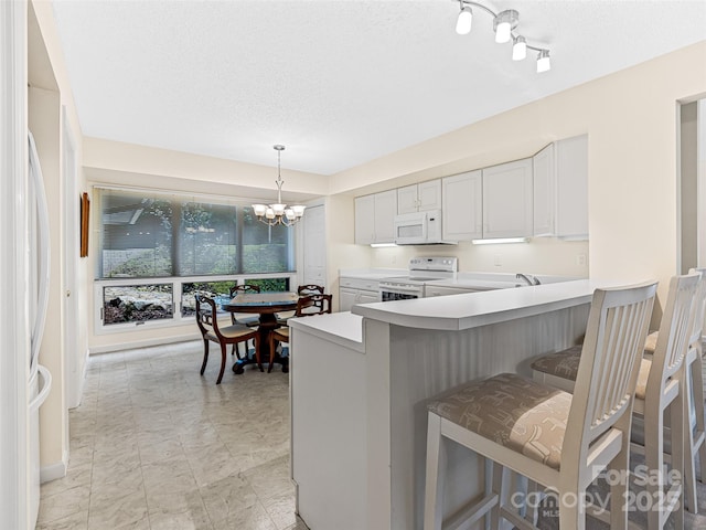 kitchen with a kitchen breakfast bar, an inviting chandelier, light countertops, white appliances, and hanging light fixtures