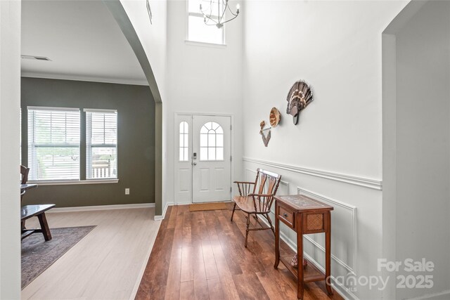 foyer with visible vents, wood finished floors, baseboards, arched walkways, and a notable chandelier