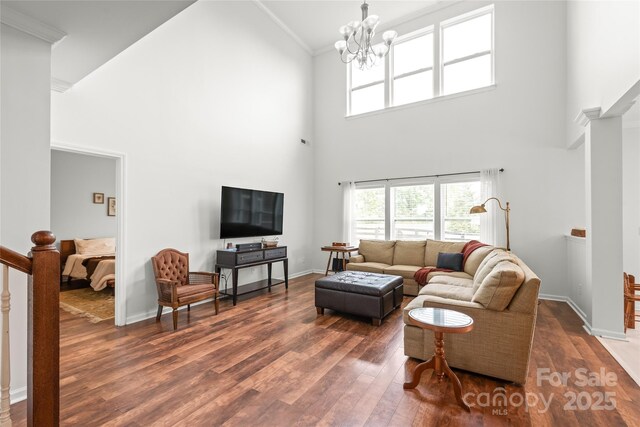 living area with crown molding, a high ceiling, an inviting chandelier, baseboards, and dark wood-style floors