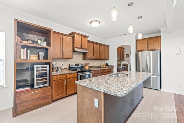 kitchen with brown cabinets, appliances with stainless steel finishes, a sink, beverage cooler, and arched walkways