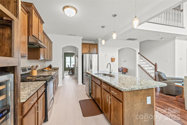 kitchen featuring a sink, light wood-type flooring, under cabinet range hood, arched walkways, and stainless steel appliances