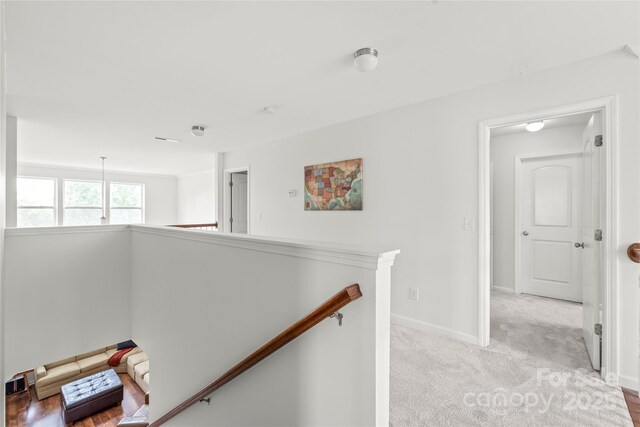 hall with light colored carpet, baseboards, and an upstairs landing