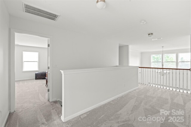 corridor featuring carpet floors, visible vents, a healthy amount of sunlight, and an upstairs landing